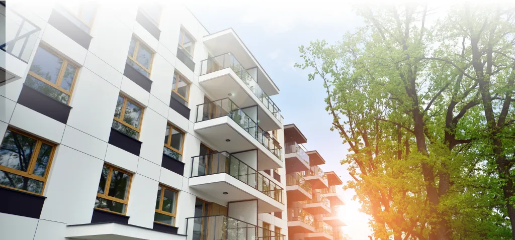 Moderne Mehrfamilienhäuser mit Glasbalkonen und Bäumen im Sonnenlicht