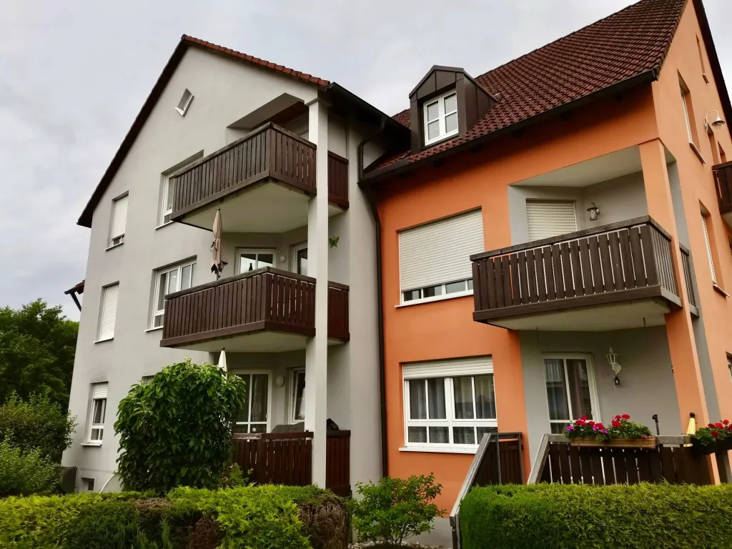 Mehrfamilienhaus mit orangefarbener und cremefarbener Fassade, Balkonen und Satteldach