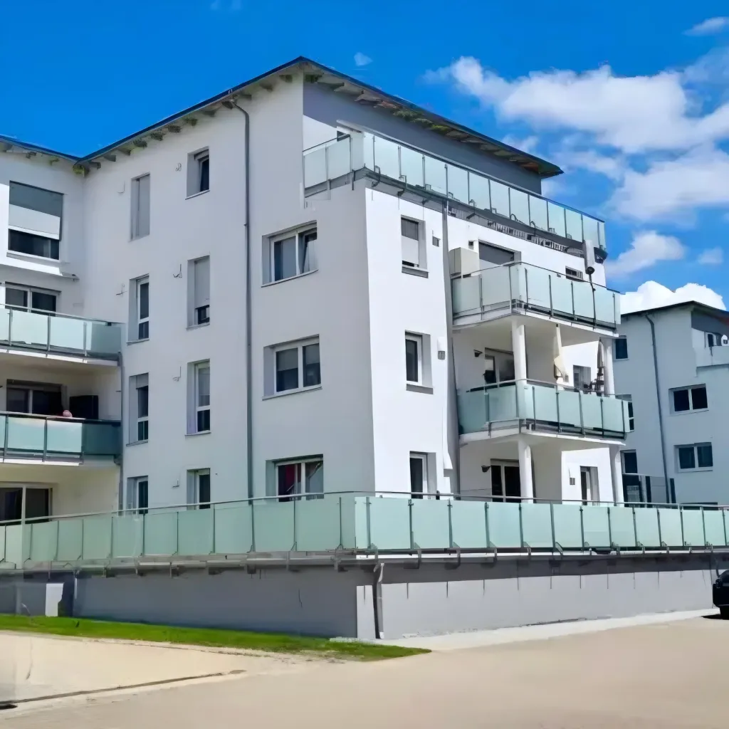 Helles Mehrfamilienhaus mit Glasbalkonen und Satteldach unter blauem Himmel