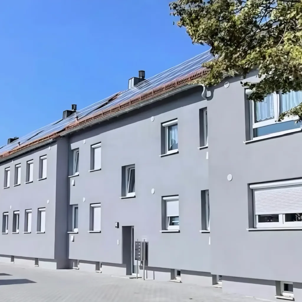 Graue Mehrfamilienhauszeile mit Solaranlage auf dem Dach an einer sonnigen Straße