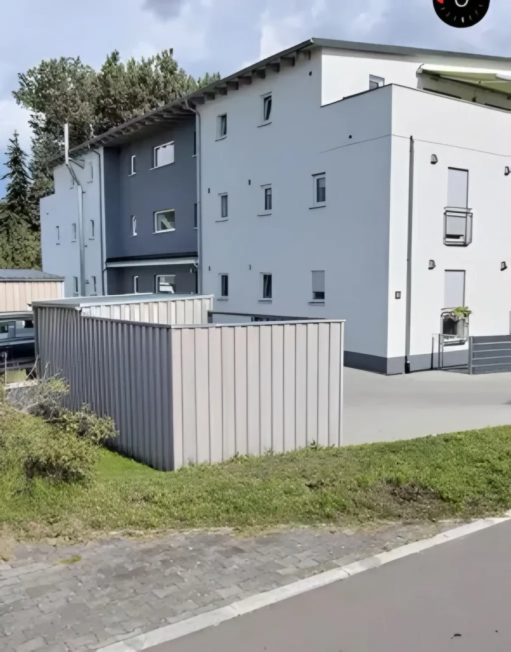 Weiß-graues Mehrfamilienhaus mit Mülltonnenverschlag und begrünter Vorfläche